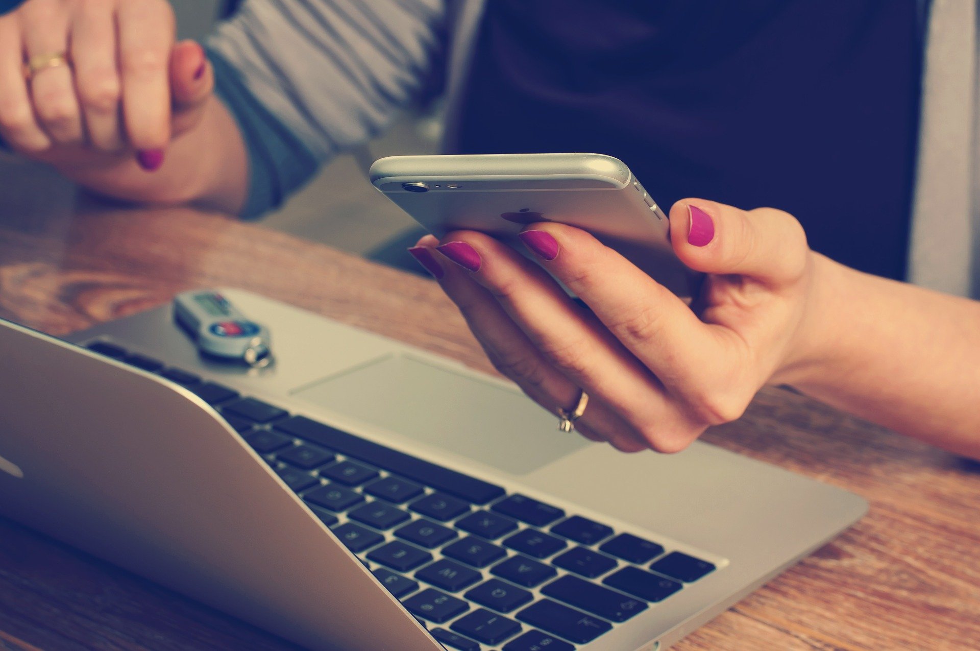 Person's hands holding a smartphone and sitting in front of a laptop computer.