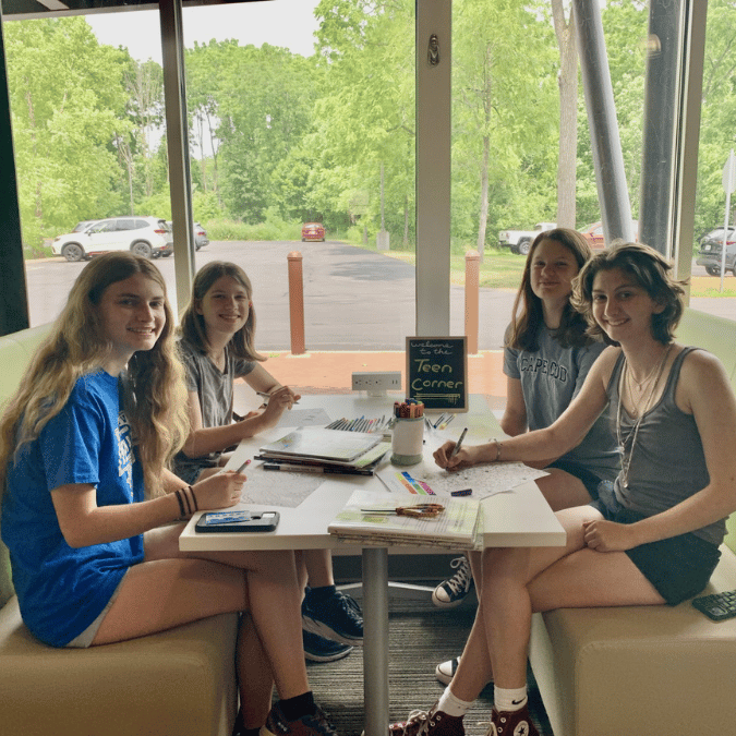 4 teenagers seated in the Mendon Public Library Teen Area.